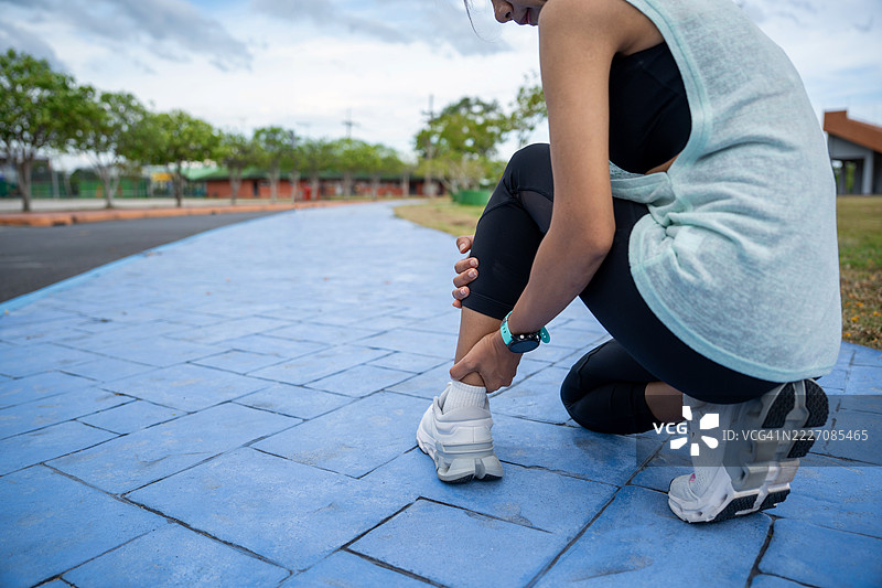 女性用手握住跟腱，因疼痛而痛苦。运动锻炼时脚踝扭伤意外，跑步时跟腱受伤。户外跑步时的跟腱损伤。图片素材