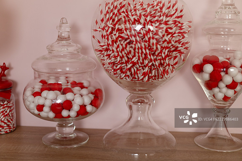 各种玻璃罐装满红色和白色的球形糖果，旁边有条纹吸管，放在木质表面上。图片素材
