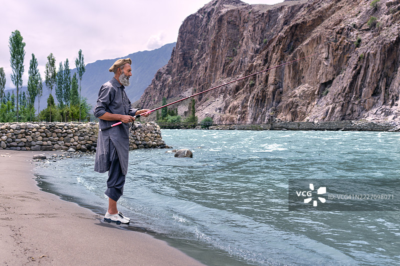 成熟男子在巴基斯坦的吉尔吉特河钓鱼，手持钓竿。图片素材
