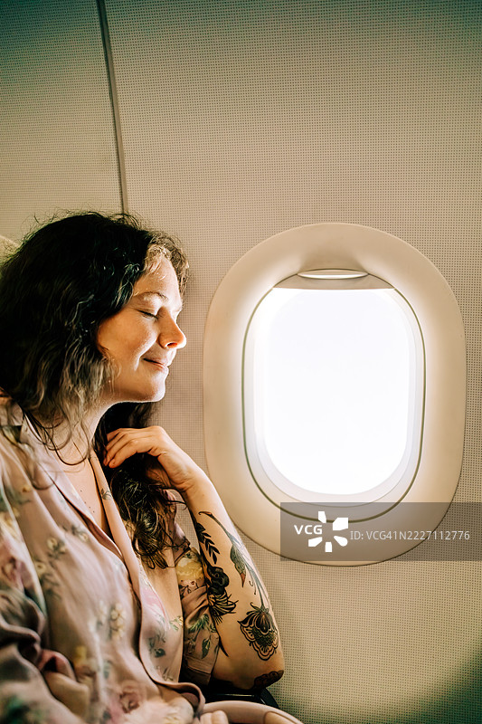 宁静的女性乘客在飞机窗边享受阳光明媚的景色图片素材