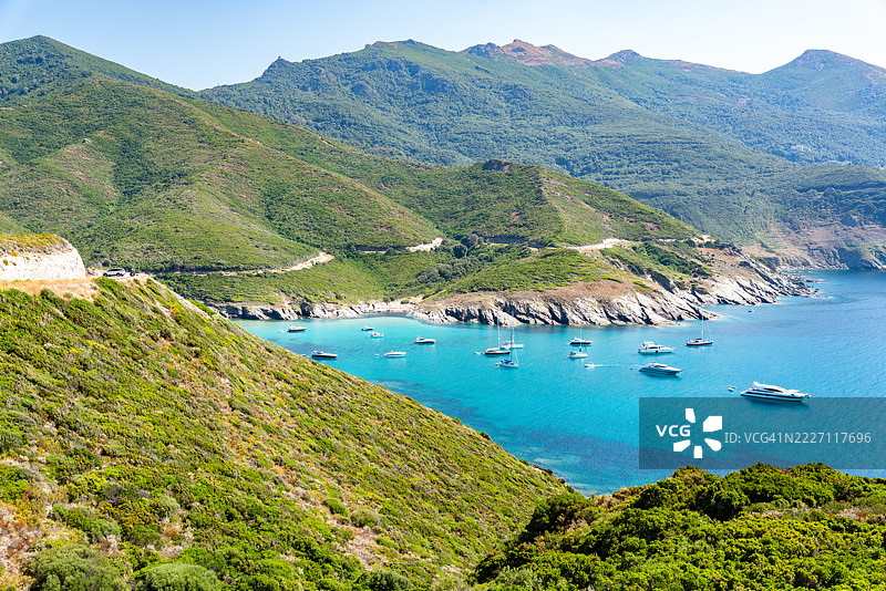 船只停泊在科西嘉海岸的碧绿海水中，四周被绿色山丘环绕。图片素材
