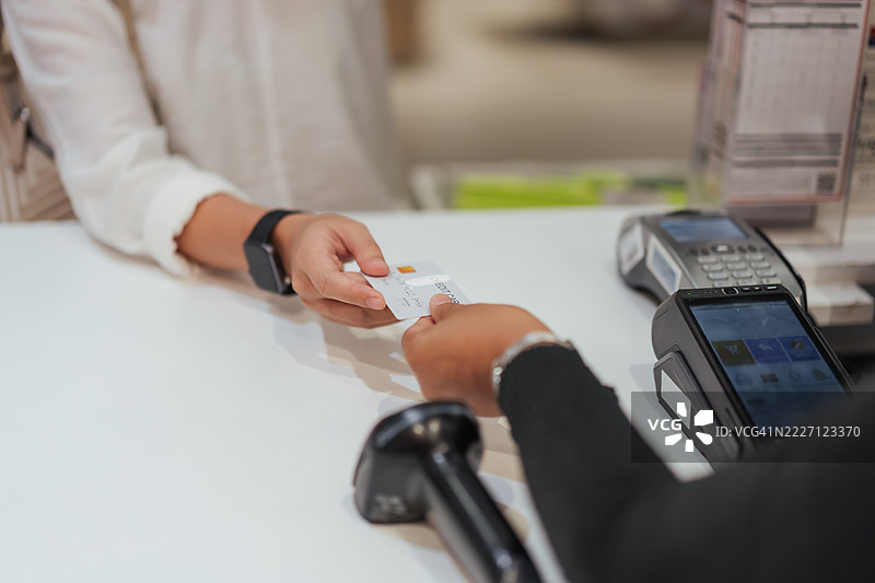 女性在零售柜台付款时将信用卡递给收银员的特写，背景中有POS终端和扫描仪，展示了现代购物和金融交易的瞬间。图片素材