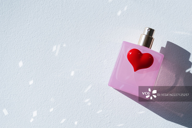 明亮的粉红色香水瓶，带有心形瓶盖，静静地放在浅色表面上，捕捉柔和的光线反射。图片素材