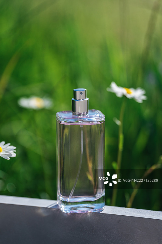 优雅的香水瓶被野花环绕，置于阳光明媚的绿草地上图片素材