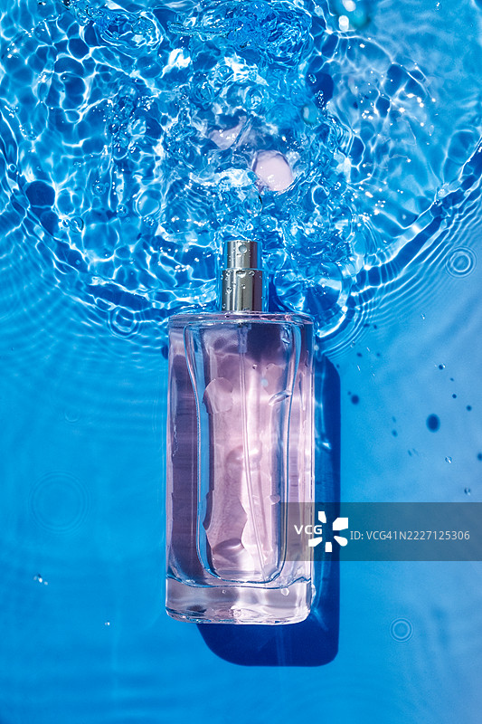 香气四溢的香水瓶沉浸在清澈的蓝色水中，水面泛起涟漪。图片素材