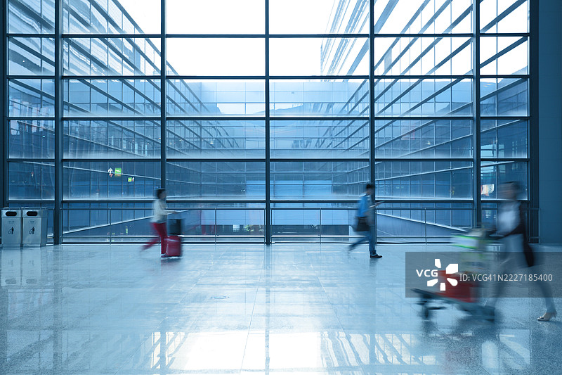 在机场的自动人行道上走动的旅客，行李在身边，主体模糊不清。图片素材