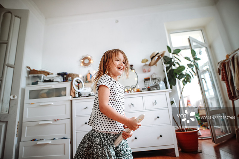 快乐的舞蹈：小女孩穿着长裙，用扫帚把清洁变成有趣的活动。图片素材