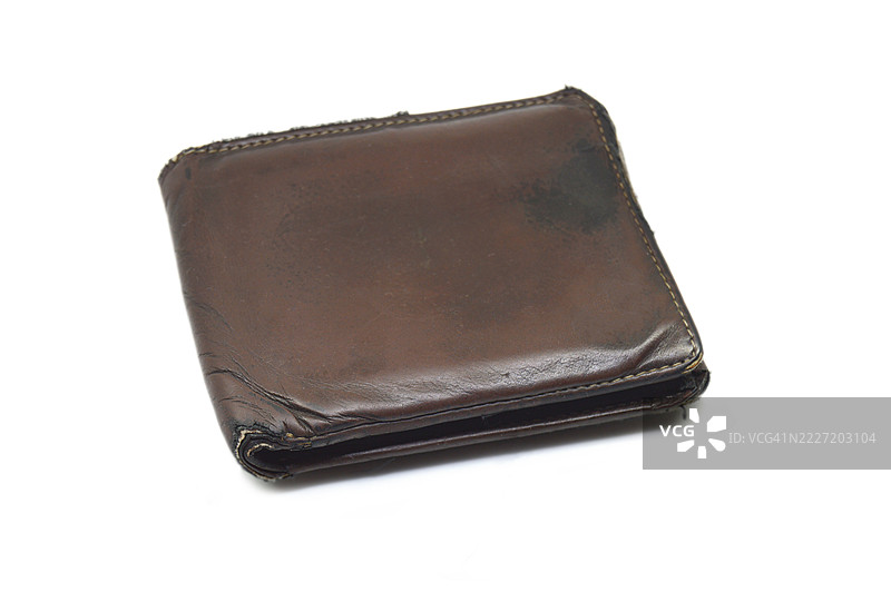 一只封闭的、倾斜的、陈旧的、磨损的、肮脏的、破旧的深棕色男士钱包或皮革口袋钱包，孤立在白色背景上。图片素材