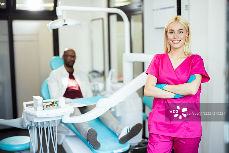 微笑的牙医在牙科诊所摆姿势，双臂交叉。图片素材