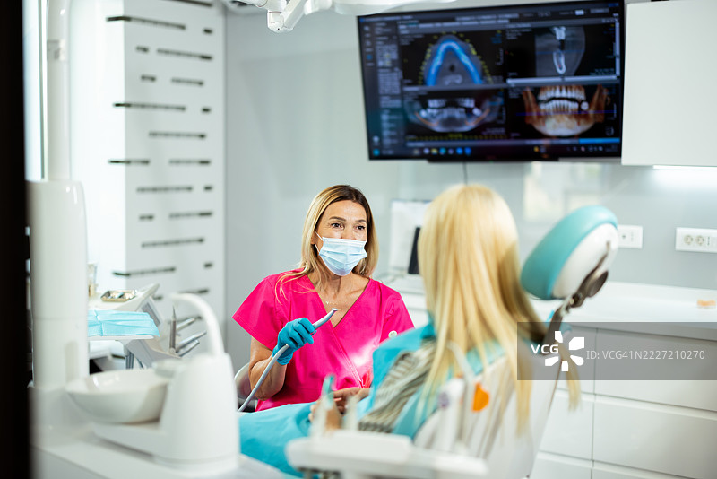 牙医在牙科诊所向患者解释治疗方案，查看显示器上的放射影像。图片素材