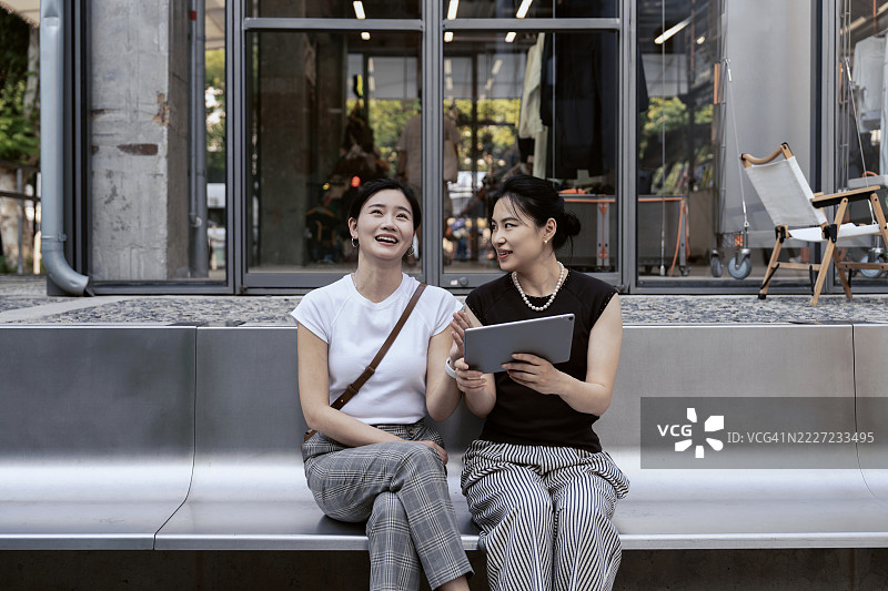 两位亚洲女性在商业区用平板电脑交谈。图片素材