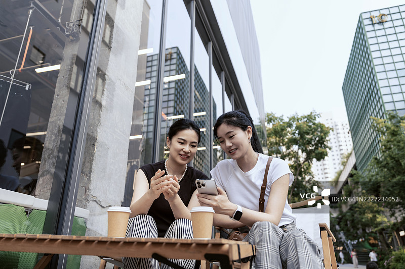 两位亚洲女性在商业区用智能手机交谈。图片素材