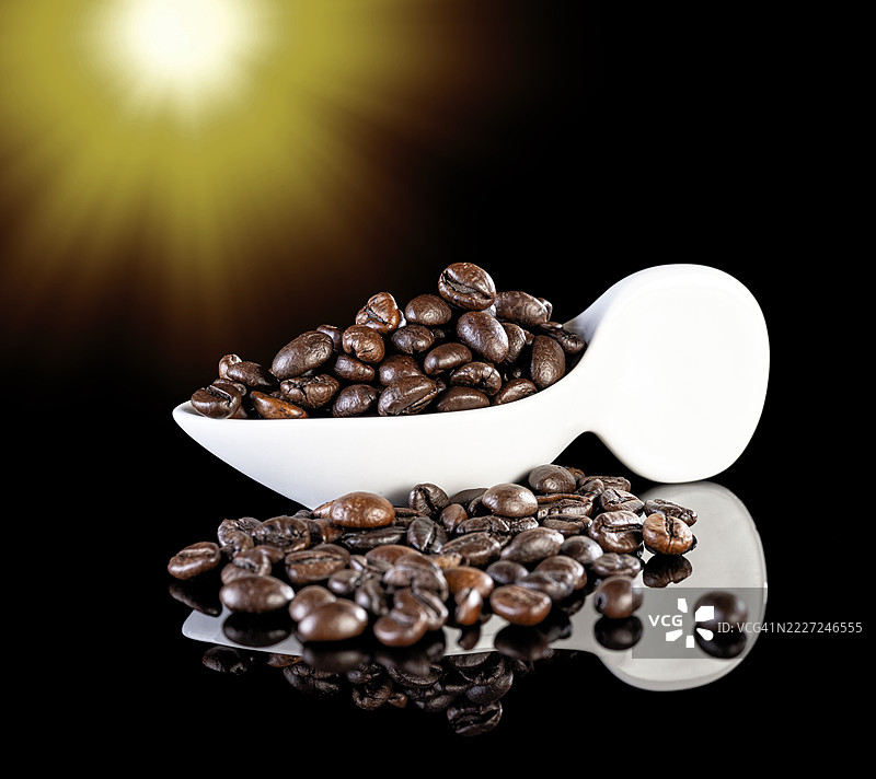 阳光照射下，黑色背景中瓷勺里的烘焙咖啡豆。图片素材