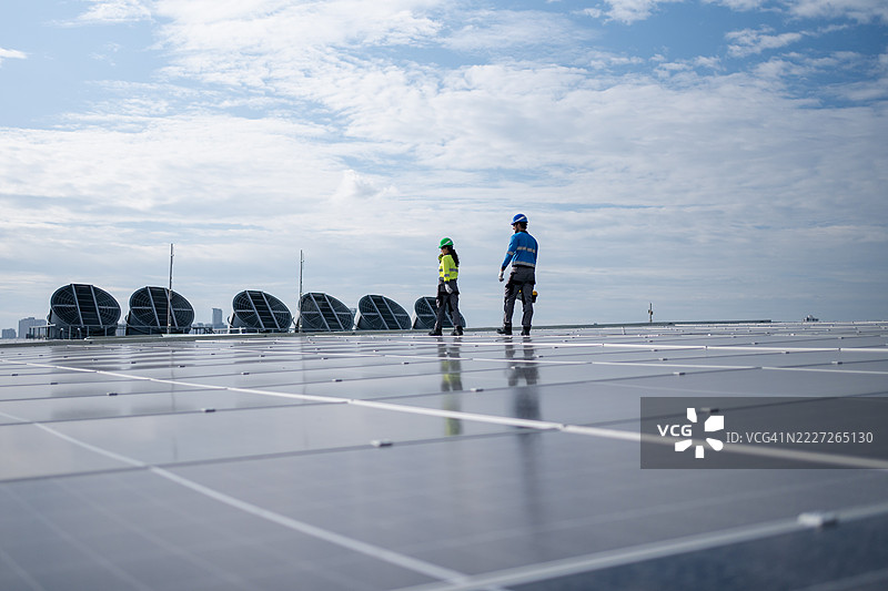 服务工程师正在检查屋顶太阳能电池板的维护情况，并检查是否有损坏的部件。技术人员还参与太阳能电池板的安装，推广清洁能源的使用。图片素材