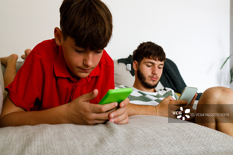 无聊的少年男孩在手机上滑动浏览图片素材