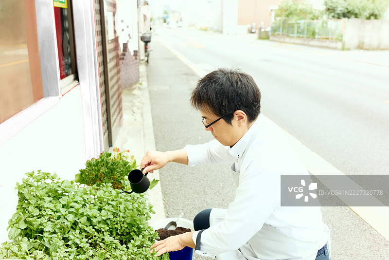 经营咖啡豆店的男子在店外施肥和浇水他的堆肥，并照顾他的室内植物。图片素材