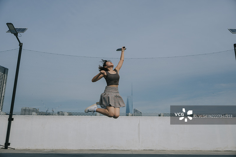 自信的年轻中国女性在屋顶球场上打皮克球时跳起。图片素材