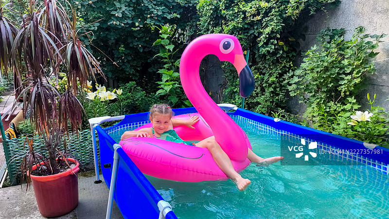 女孩在后院游泳池的粉色火烈鸟浮筒上放松。图片素材