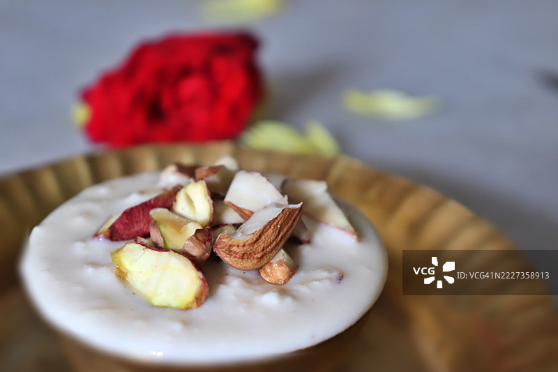 自制拉布里/拉布迪/拉比迪，一道用牛奶制成的甜点，顶部装饰有杏仁和开心果，放在铜碗中/玫瑰花/贾纳马什特米节图片素材