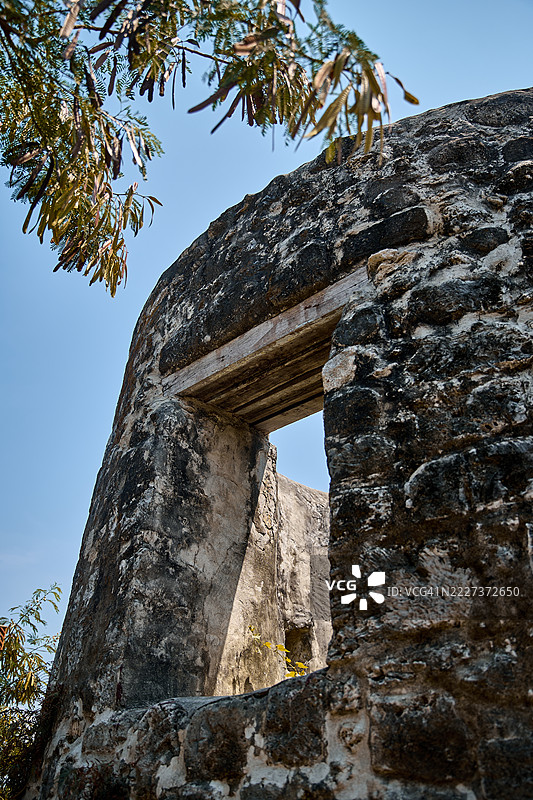 古老石头遗迹的特写，窗户般的开口被悬垂的树枝框住。图片素材