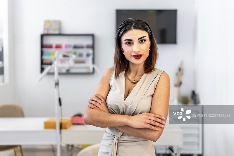 一位年轻的女企业家，双手交叉放在头上，身处美发美容沙龙，展现出自信专业的风采。图片素材