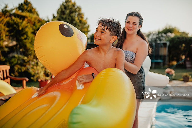 年轻男孩在夏日的游泳池中快乐地嬉水，身边有一个开心的成年人和浮筒。图片素材