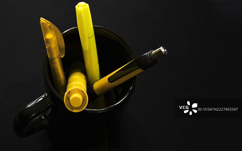 四支黄色的笔放在一个黑色的杯子里，背景是黑色的。图片素材