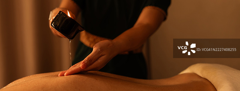 专业按摩师的手上特写按摩蜡烛，正在将融化的按摩蜡烛中的温暖油倒在顾客的背上，进行放松的水疗护理。图片素材