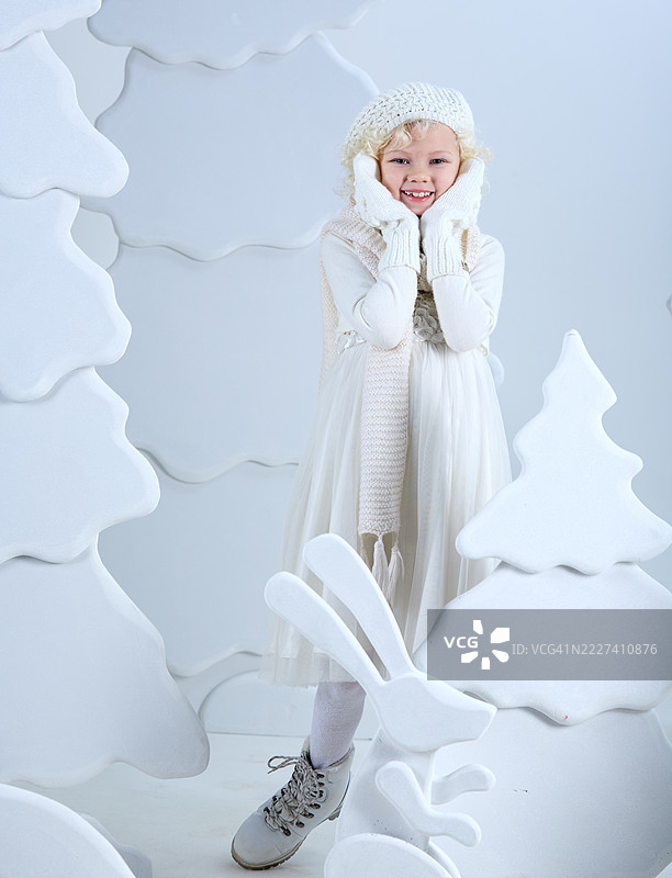 美丽的金发女孩站在白色的仙境森林中，微笑着看向镜头，双手托着脸颊。圣诞童话。图片素材