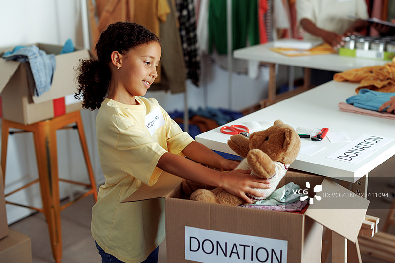 年轻女孩志愿者将泰迪熊放入捐赠箱中图片素材