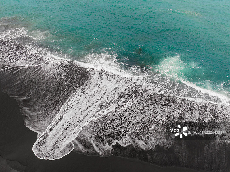 航拍图像显示来自印度洋的延伸波浪流经印度尼西亚巴厘岛克伦贡区的黑沙滩图片素材