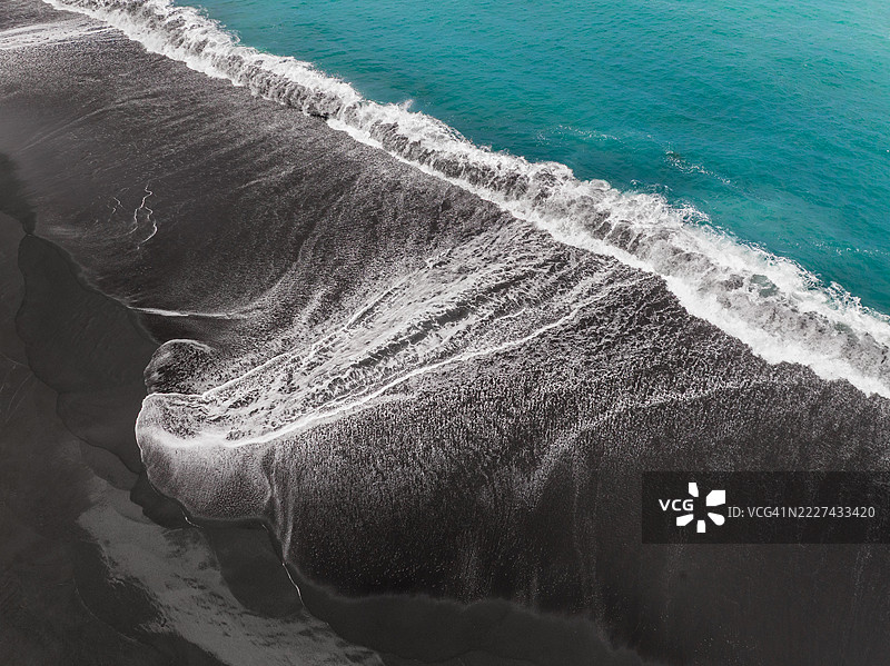 航拍照片显示一条延伸的海浪在印度尼西亚巴厘岛克伦贡区的火山海滩上涌动。图片素材