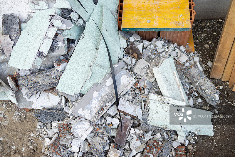 一堆建筑废料和碎石，包括破碎的混凝土、砖块和带有网状加固的石膏，散落在地面上。图片素材