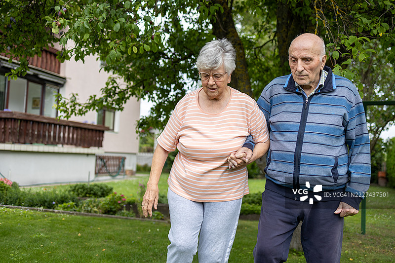 一位老人扶着一位老妇人在花园里一起散步。老年人的关系图片素材