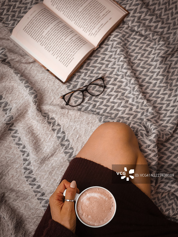 俯视视角，一名女子在床上拿着咖啡杯和书籍，波兰奥尔什丁图片素材