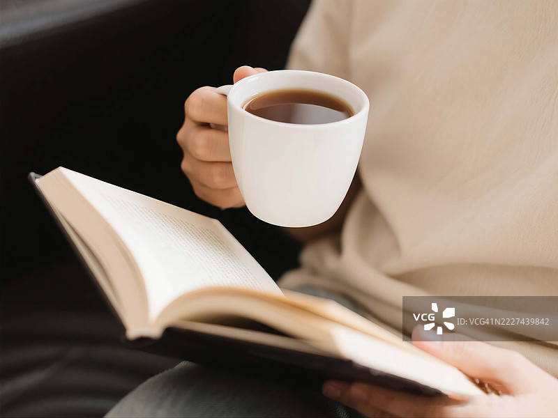 马来西亚一名女性在床上阅读书籍时手持咖啡杯的中段特写图片素材