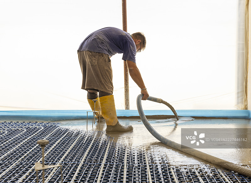 新建建筑中，男子正在新建筑的混凝土地板采暖系统上浇筑混凝土，现代建筑系统，布林迪西，普利亚，意大利图片素材