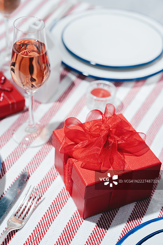 红色礼品盒，上面系着丝带，放在带餐具的盘子上。桌子，条纹桌布。俯视图。样机。图片素材