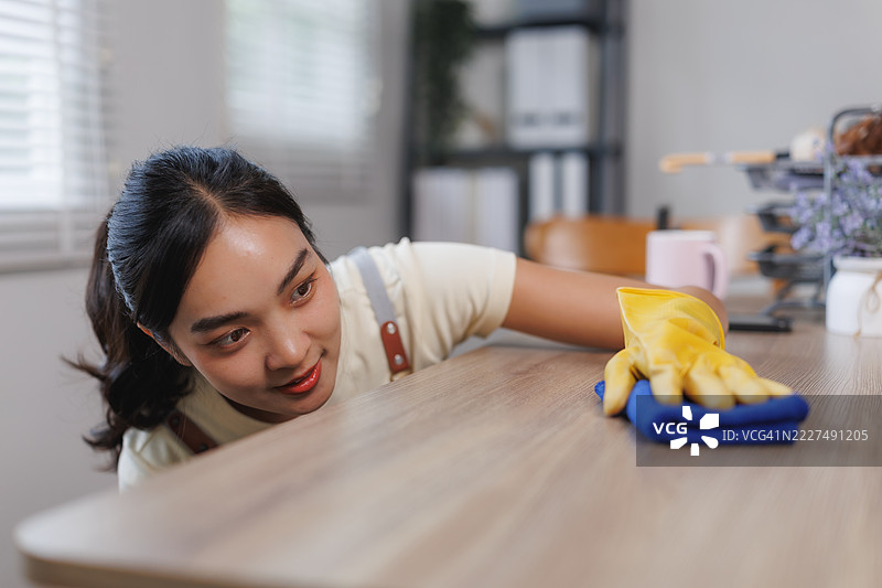 年轻女性戴着手套，用超细纤维布擦拭桌子图片素材