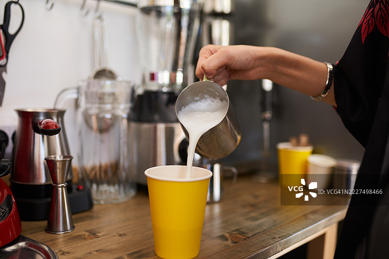 在咖啡馆里将蒸汽牛奶手工倒入明亮的黄色杯子中图片素材