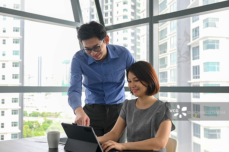 亚洲男性经理在员工的办公桌前教授记账知识。图片素材