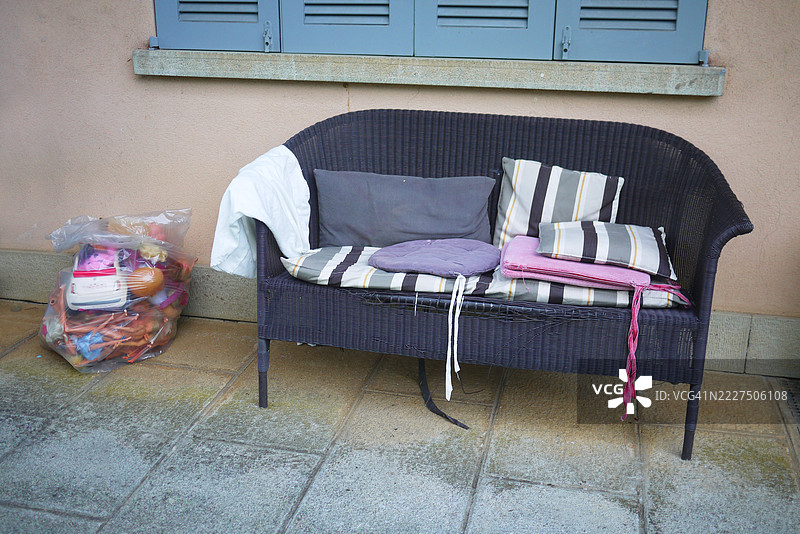 黑色藤编长椅，前面有靠垫，靠在墙边图片素材
