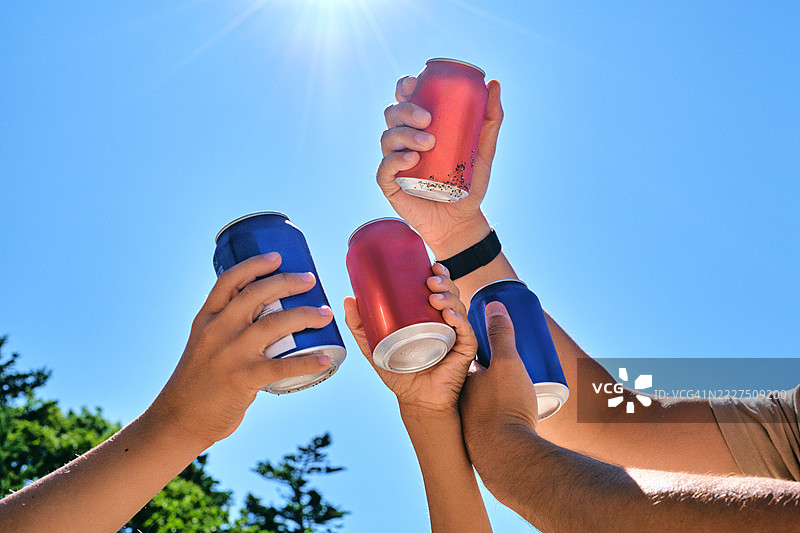 手握不同罐装碳酸饮料，背景是天空。图片素材