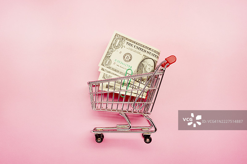 高角度视图的小购物车和美元钞票在粉色背景上图片素材