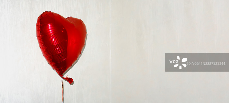 红色光泽心形气球在明亮的角落环境中。适合任何庆祝活动或事件的欢乐与爱。图片素材