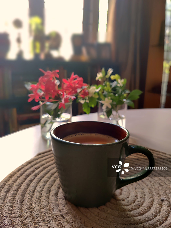 陶瓷杯中的早晨茶，放在黄麻垫上，旁边有红色的千日红和新鲜的橙花，体现了正念与慢生活。图片素材
