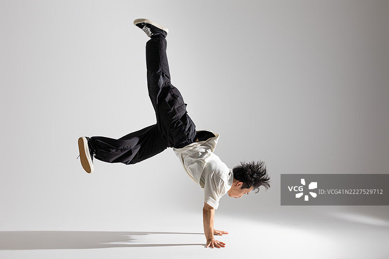 在摄影棚中，年轻的亚洲男性街舞者在白色背景下表演杂技。图片素材