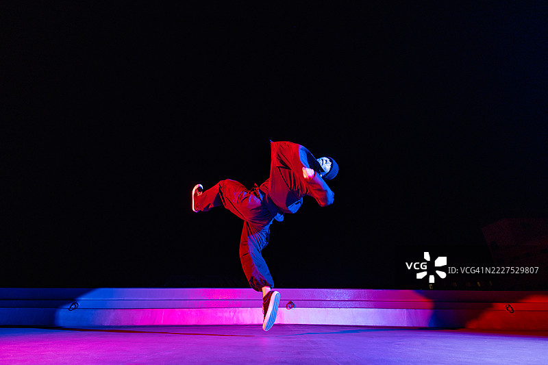 屋顶上的霓虹灯光效果下的霹雳舞表演。年轻的亚洲男性。图片素材