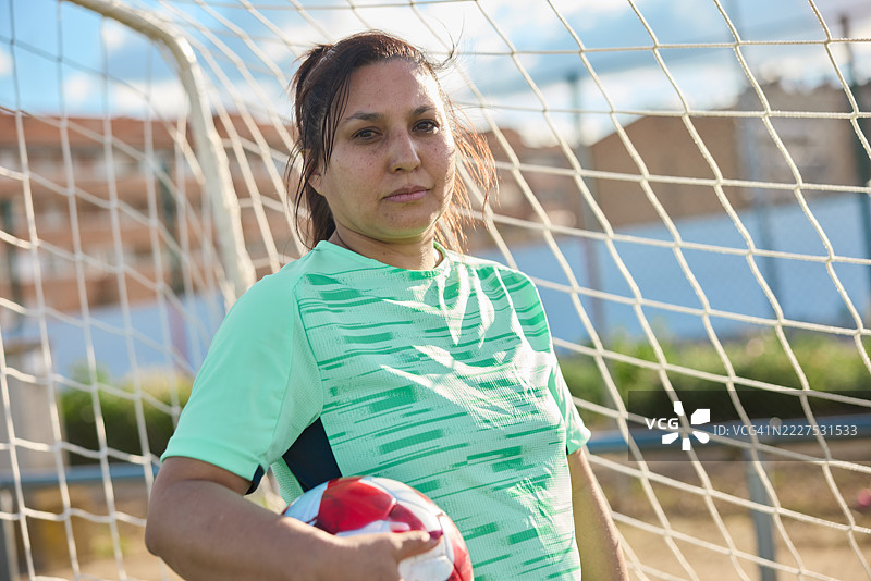 一位穿着运动服的女足球运动员的肖像，手臂下夹着一个足球。图片素材