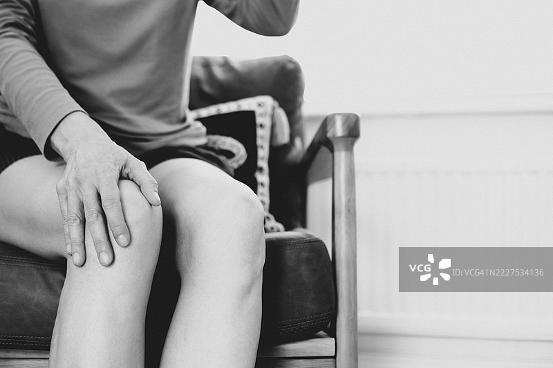 一位女性坐在沙发上，揉搓膝盖以缓解腿部疼痛或紧张。图片素材